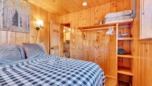 A wooden cabin room with a bed, a shelf with folded towels, and a painting of a forest on the wall. - Monteverde Getaway (Cabin 106) (Greer)