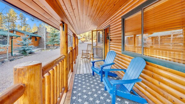 A wooden cabin with a porch, blue Adirondack chairs, and a view of the surrounding forest. - Monteverde Getaway (Cabin 106) (Greer)