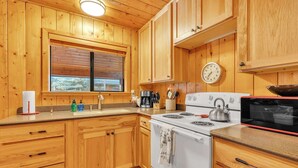 A wooden cabin kitchen with a stove, sink, and a clock on the wall. - Monteverde Getaway (Cabin 106) (Greer)