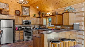 Une cuisine de style rustique, avec des meubles en bois, des appareils électroménagers en acier inoxydable, un coin bar avec des tabourets et un lustre.