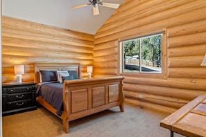 A log cabin bedroom with a wooden bed, bedside tables, and a window with a view of trees. - Little Colorado Lodge (Cabin 175) (Greer)