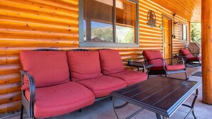 A log cabin with a covered porch, a red sofa, and two chairs. - Cowboy Casita (Cabin 102) (Greer)