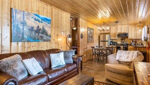 A cozy cabin interior with a wooden interior, a leather sofa, a dining area, and a kitchen. - Cowboy Casita (Cabin 102) (Greer)