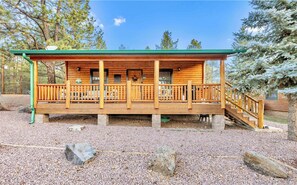 Une cabane en bois dotée d’un porche, d’une terrasse couverte et de fondations en pierre.