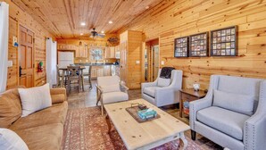 A wooden interior with a sofa, chairs, a coffee table, a kitchen area, and framed pictures on the wall. - Monteverde Retreat (Cabin 104) (Greer)
