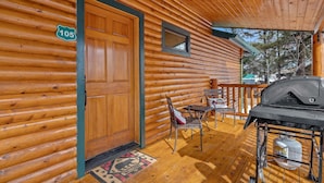 A wooden cabin with a number '105' sign, a covered porch with a grill, and a dining area with chairs and a table. - Black Bear Chalet (Cabin 105) (Greer)