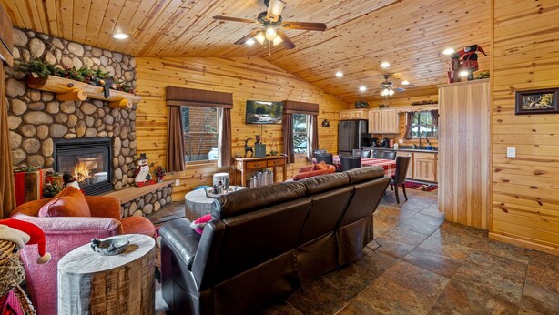 A cozy log cabin interior with a stone fireplace, leather sofa, and a kitchen area. - Black Bear Chalet (Cabin 105) (Greer)
