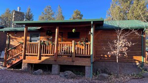 A log cabin with a wooden porch, a stone chimney, and a green roof. - Black Bear Chalet (Cabin 105) (Greer)
