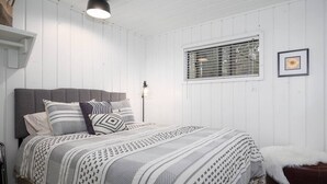 A bedroom with a bed, a window with blinds, a hanging light fixture, and a framed picture on the wall. - Aspen Cabin 1 (Greer)