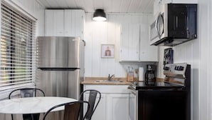 A compact kitchen with white cabinetry, a stainless steel refrigerator, a microwave, and a coffee maker. - Aspen Cabin 2 (Greer)