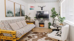 A cozy living room with a sofa, a white armchair, a fireplace, and a television. - Cowgirl Cabin (Aspen 3) (Greer)