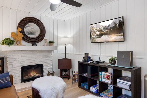 A living room with a fireplace, a television mounted on the wall, a bookshelf, and a decorative rooster statue.
