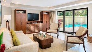 Un salon moderne avec un canapé, des fauteuils, une table basse et un téléviseur. On peut apercevoir une piscine à travers les portes vitrées.