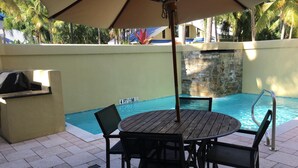 Un espace aménagé au bord de la piscine, avec une table ronde et des chaises, un barbecue et un mur en pierre.