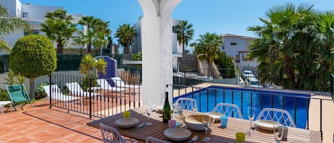 Un área de comedor al aire libre cubierta con vistas a una piscina y villas.