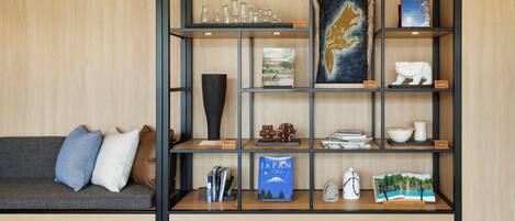 Un interior moderno con un panel de madera, un sofá gris con cojines y un estante metálico negro que exhibe diversos objetos decorativos y libros.
