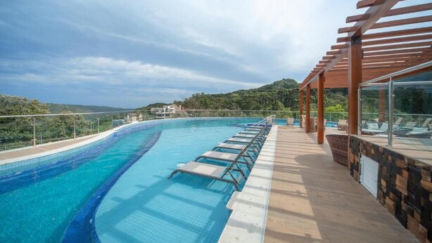 A curved infinity pool with lounge chairs and a pergola overlooking a mountainous landscape. - GOLDEN GRAMADO RESORT LAGHETTO (Gramado)
