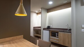 A compact kitchen with a dining area, including a table and chairs, a refrigerator, and a microwave. - GOLDEN GRAMADO RESORT LAGHETTO (Gramado)