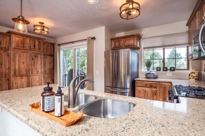 A kitchen with granite countertops, stainless steel appliances, wooden cabinets, and pendant lighting.