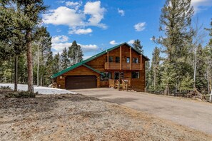 A two-story log cabin with a green roof, a front garage, and a balcony.