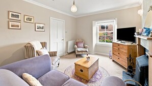 Un salon comprenant un canapé, un fauteuil, une commode en bois et un téléviseur.