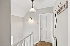 Een trap met een witte deur aan de bovenkant, een lamp erboven en een wandlamp aan de linkerkant.