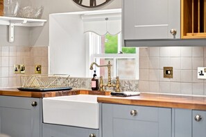 Une cuisine dotée d’un plan de travail en bois, d’un robinet de style rétro et d’une fenêtre donnant sur un paysage verdoyant.