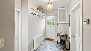 Un couloir avec un radiateur, un tapis à motifs, un porte-manteau, une porte avec une fenêtre et un luminaire au plafond.