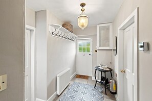 A hallway with a radiator, a patterned rug, a coat rack, a door with a window, and a ceiling light fixture.