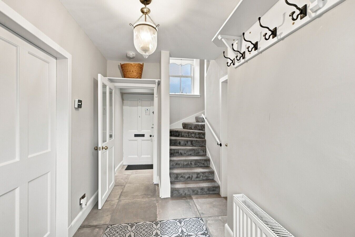 A hallway with a white door, a basket on the wall, a staircase with a handrail, and a radiator.