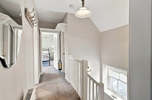 A hallway with a carpeted floor, white walls, a white railing, and a window on the right.