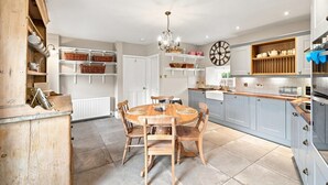 Une cuisine avec une table ronde en bois, des placards blancs et une horloge au mur.