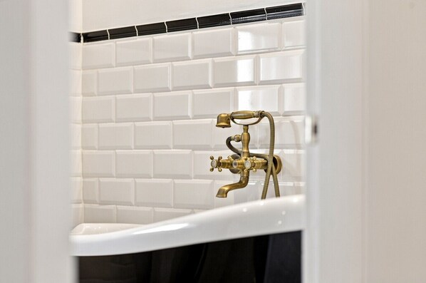 A bathroom with a white bathtub, a brass faucet, and a tiled wall.