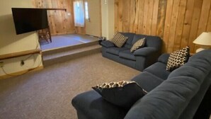 A living room with a dark blue sofa, a flat-screen TV, and a wooden wall.