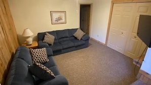 A living room with a dark blue sofa, patterned cushions, a lamp, and a ceiling fan.