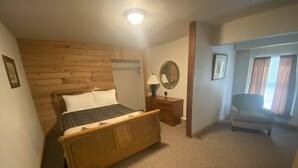 A bedroom with a wooden headboard bed, a nightstand with a lamp, a chair, and a window with curtains.