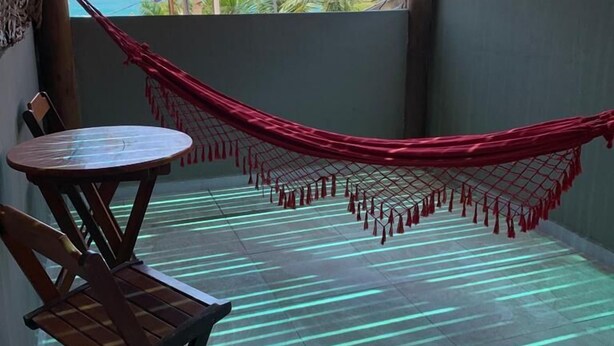 A balcony with a hammock, a wooden table, and chairs. - Clara Lua Suites (Ipojuca)