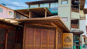 A two-story building with a wooden facade, a balcony on the upper floor, and a small shop entrance with a sign. - Clara Lua Suites (Ipojuca)