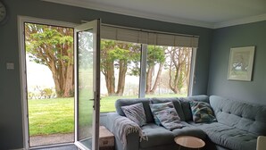 Een moderne woonkamer met een grijze bank, een klein rond tafeltje en een schuifdeur naar een tuin.