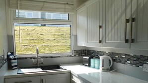 Een keuken met witte kastjes, een raam met uitzicht op een grasveld, een spoelbak en een waterkoker op het aanrecht.