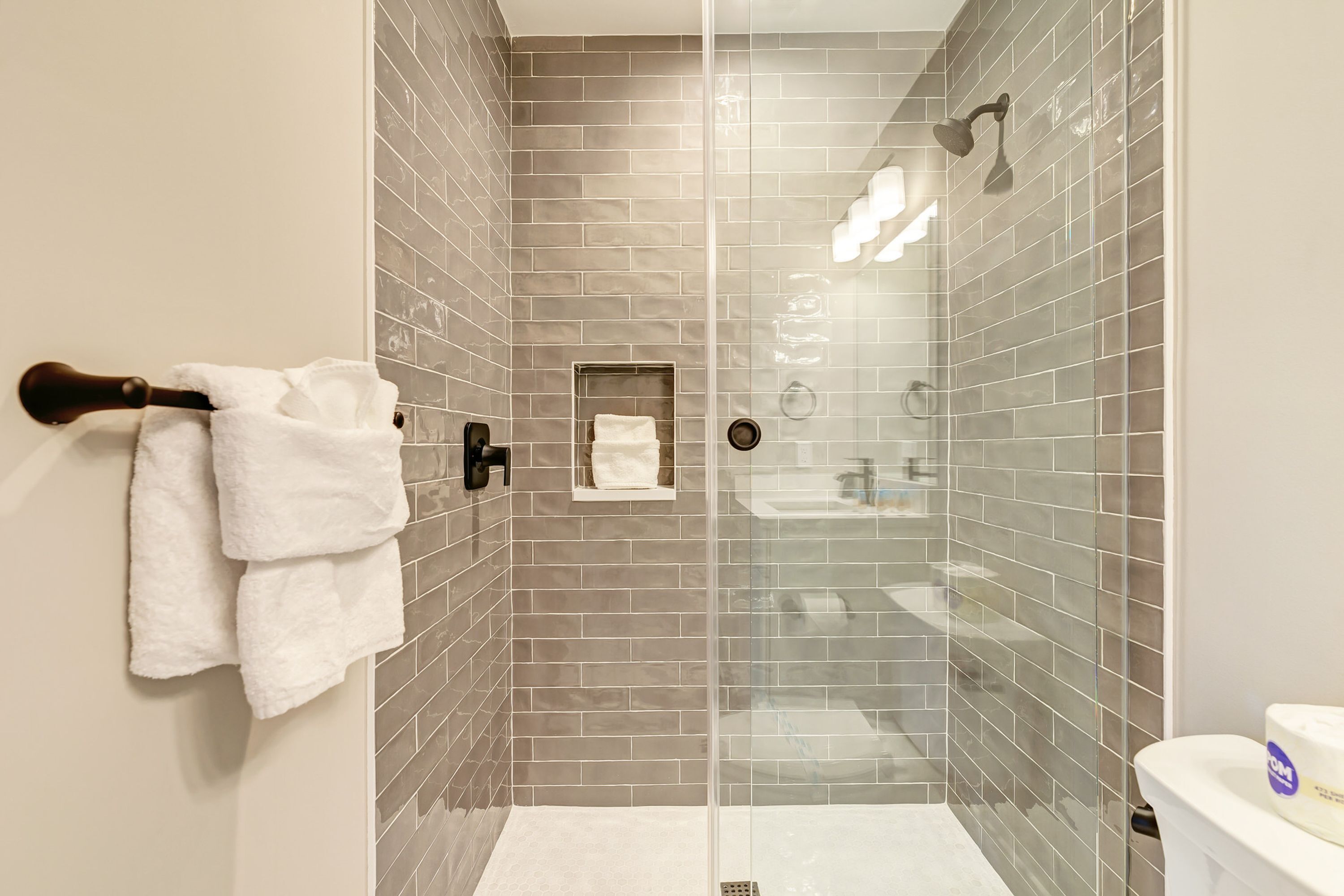 Ein modernes Badezimmer mit Duschkabine aus Glas, einem Handtuchhalter mit weißen Handtüchern und einer sichtbaren Toilette.