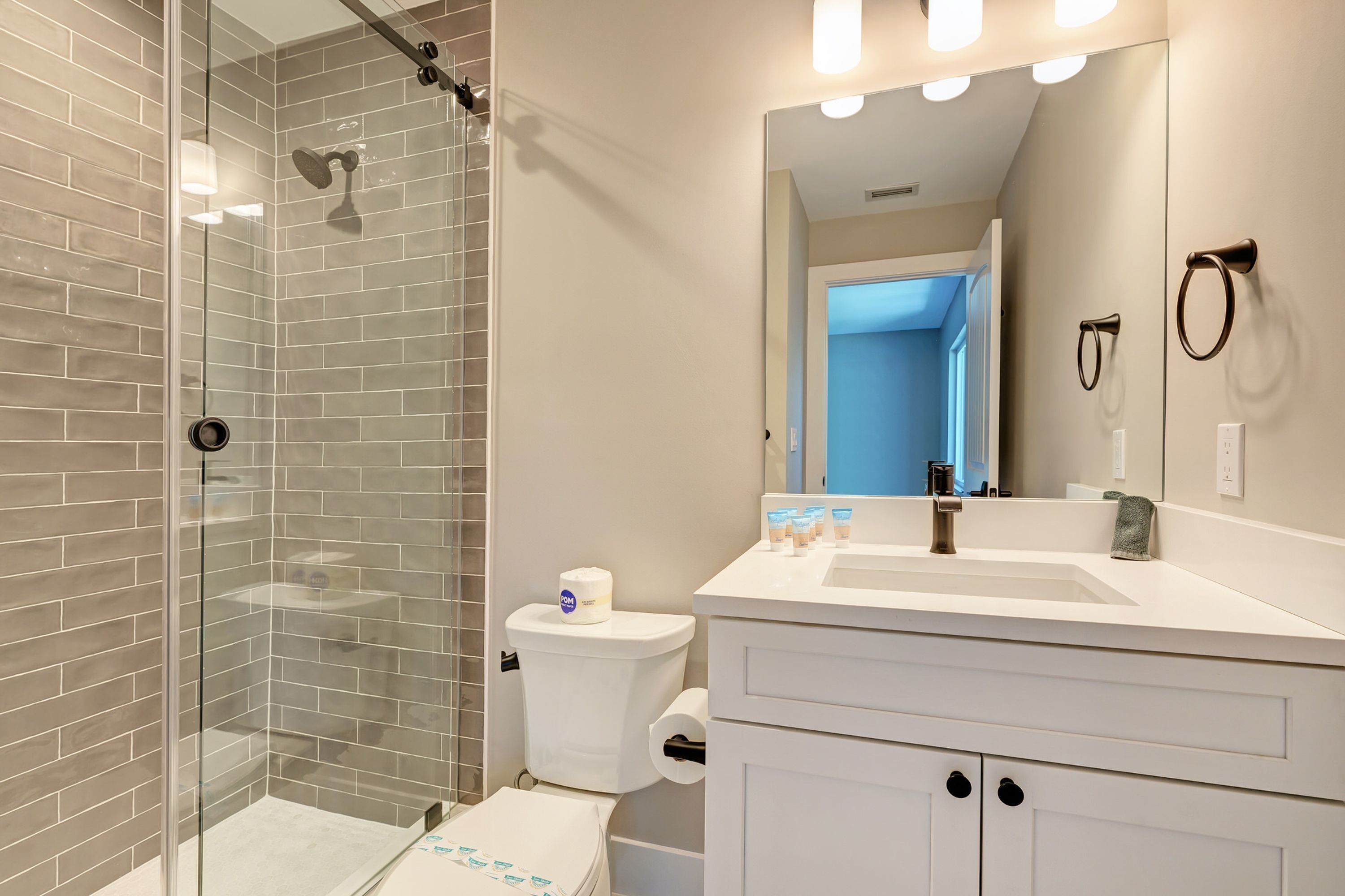 Une salle de bain moderne avec une douche à parois de verre, des toilettes blanches et un meuble-lavabo avec un miroir.