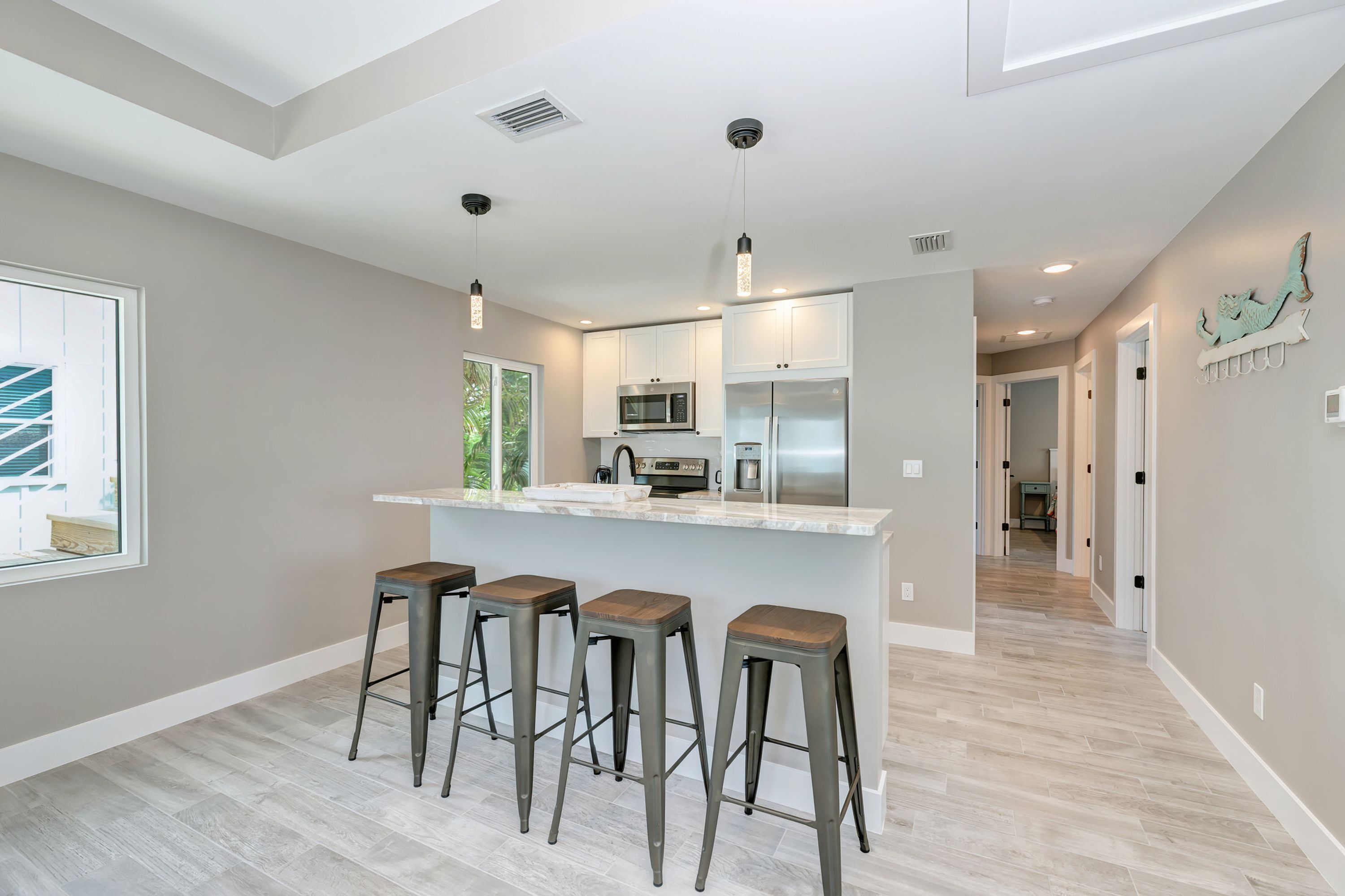 A modern kitchen with a central island, bar stools, and a view of the outdoors.