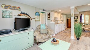 Un salon avec un téléviseur, un fauteuil à motifs, une table vert clair et un poisson décoratif accroché au mur.