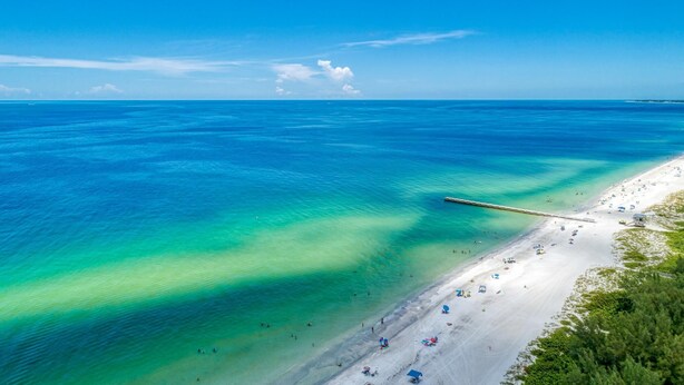 Une plage aux eaux turquoise et limpides, bordée d’un rivage sablonneux.