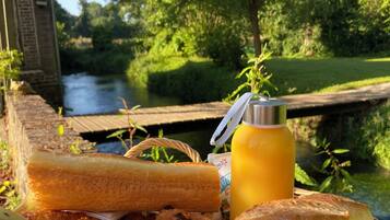 A basket of food items including bread, a banana, and a bottle of juice, placed outdoors with a river and greenery in the background.