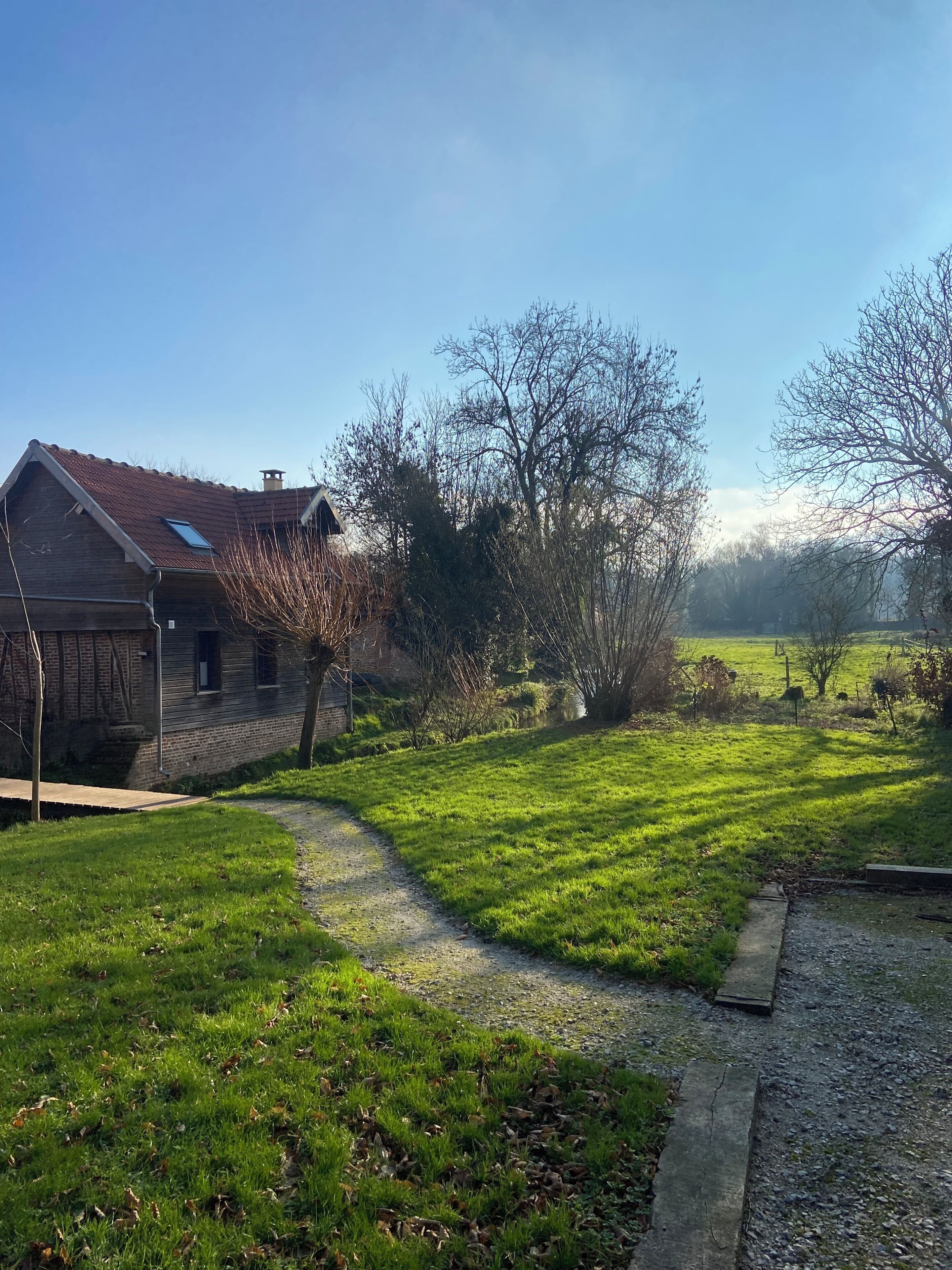 A rural property with a stone house, a gravel path, and a grassy field.