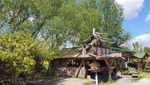 A rustic wooden structure with a sloped roof and a chimney, surrounded by lush greenery and trees. - Historic "Alter Bahnhof" Oberdorla with private playground, (Vogtei OT Oberdorla)