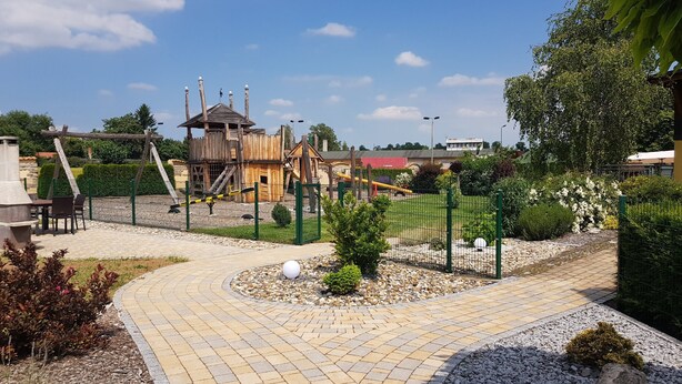 A playground area with a wooden play structure, a fenced garden, and a paved walkway. - Historic "Alter Bahnhof" Oberdorla with private playground, (Vogtei OT Oberdorla)
