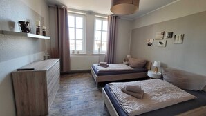 A bedroom with two beds, a dresser, a window with curtains, and a hanging lamp. - Historic "Alter Bahnhof" Oberdorla with private playground, (Vogtei OT Oberdorla)